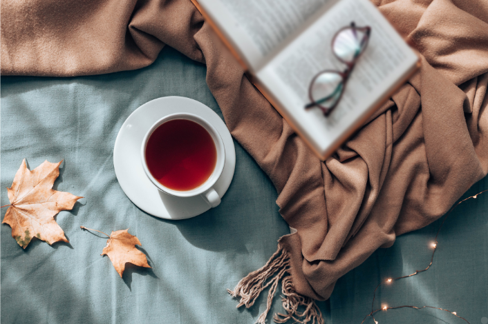 Book with glasses, warm cup of tea and a brown throw blanket